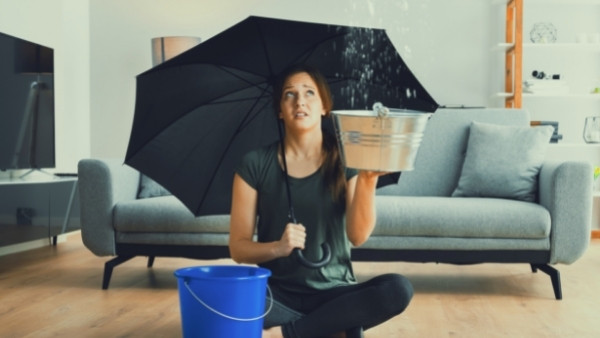 En kvinne som har vannskader i den nye boligen sin, sitter på gulvet og holder en paraply før hun skal ta kontakt med en advokat spesialisert på boligtvister